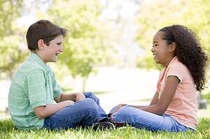 Tow young friends sitting outdoors looking at each other and smiling