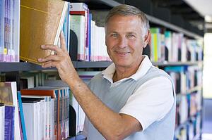 Man in library pulling book off a shelf (depth of field)
