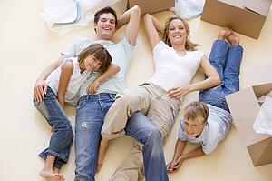 Family lying on floor by open boxes in new home smiling