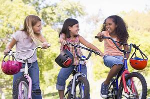Three young girl friends outdoors on bicycles smiling