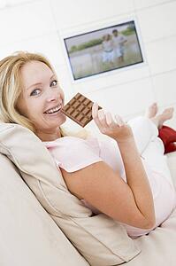Pregnant woman watching television and eating chocolate smiling