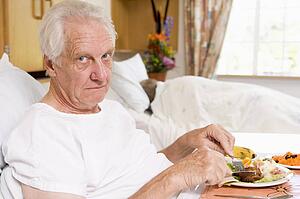 Senior Man Eating Hospital Food In Bed