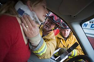 Fireman helping woman with neck brace while another fireman uses the jaws of life on a car door (selective focus)