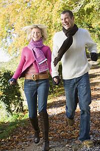 Couple running outdoors on path in park smiling (selective focus)