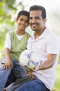 Father and son outdoors in park with ball smiling (selective focus)