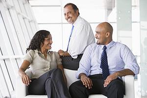 Three businesspeople sitting indoors smiling (high key/selective focus)