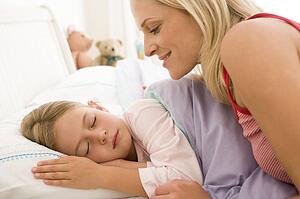 Woman waking young girl in bed smiling