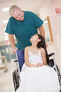 An Orderly Pushing A Little Girl In A Wheelchair Down A Hospital Corridor