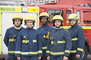Five firefighters standing by fire engine wearing helmets