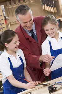 Female students reviewing woodworking plans with teacher