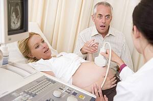 Pregnant woman getting ultrasound from doctor with husband watching
