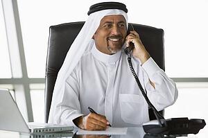 Businessman in office on telephone by laptop smiling (high key/selective focus)