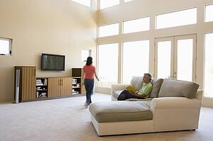 Man reading book in living room with woman walking by