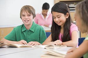 Students in class reading with teacher in background (selective focus)