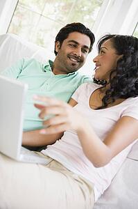 Couple in living room with laptop smiling (high key/selective focus)