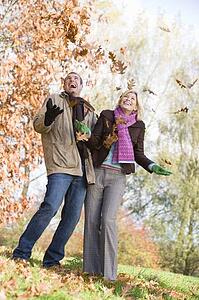 Couple outdoors playing in leaves and smiling (selective focus)