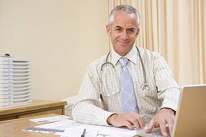 Doctor using laptop in doctor's office smiling