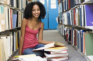 Woman sitting on floor in library holding book
