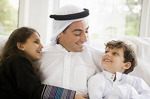 Father and two young children sitting in living room smiling (high key/selective focus)