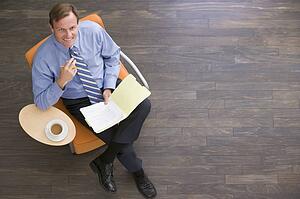 Businessman sitting indoors with coffee and folder smiling