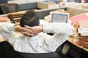 Businessman in cubicle with laptop and stacks of files