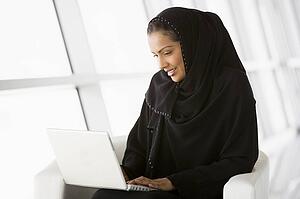 Woman sitting indoors with laptop smiling (high key/selective focus)