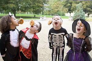 Four young friends on Halloween in costumes eating donuts hanging off strings
