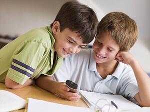 Two Young Boys Distracted From Their Homework, Playing With A Cellphone