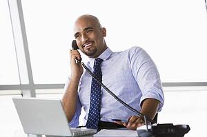 Businessman in office on telephone by laptop smiling (high key/selective focus)
