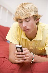 Teenage Boy Lying On Bed Using Mobile Phone 