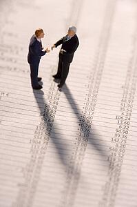 Figurines Of Two Businessmen Shaking Hands On A Financial Newspaper