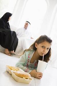 Young girl with fast food in living room with parents in background (high key/selective focus)