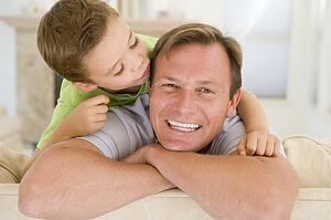 Young boy kissing smiling man in living room