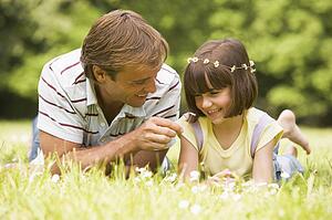 Father and daughter lying outdoors with flowers smiling