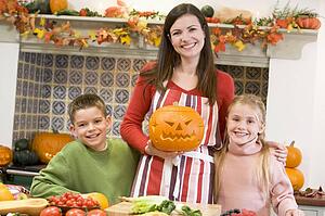 Mother and two children carving jack o lanterns on Halloween and smiling