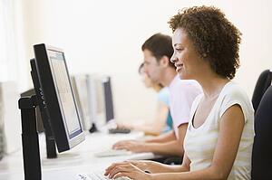 Three people sitting in computer room typing and smiling