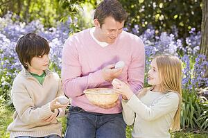 Father and two young children on Easter looking for eggs outdoors smiling