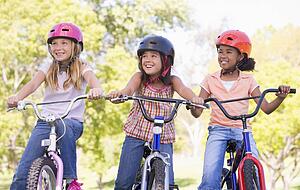 Three young girl friends outdoors on bicycles smiling