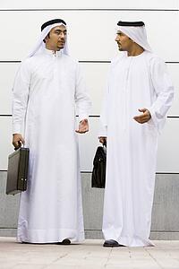 Two businessmen standing outdoors with briefcases talking