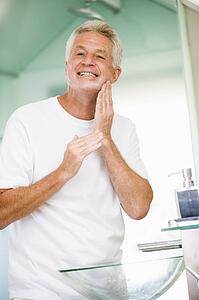 Man in bathroom applying aftershave and smiling