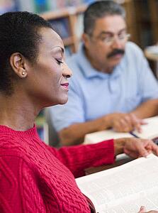 Woman sitting near man in library with books and notepads (selective focus)