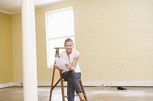 Woman sitting on ladder in empty space holding paper