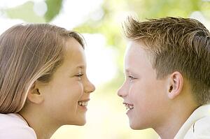 Brother and sister sitting outdoors staring at each other and smiling