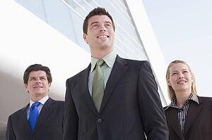 Three businesspeople standing outdoors by building smiling