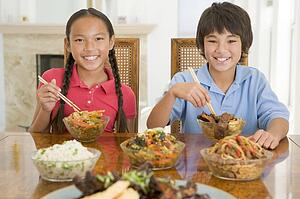 Two young children eating chinese food in dining room smiling