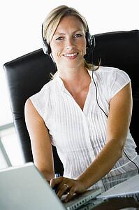 Businesswoman sitting in office wearing headset using laptop and smiling
