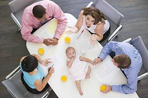 Four businesspeople in boardroom with a baby lying on the table