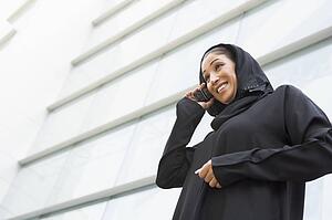 Businesswoman outdoors by building using cellular phone and smiling (selective focus)
