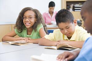 Students in class reading with teacher in background (selective focus)