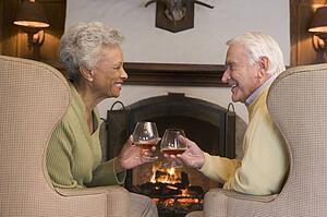 Couple sitting in living room by fireplace with drinks smiling